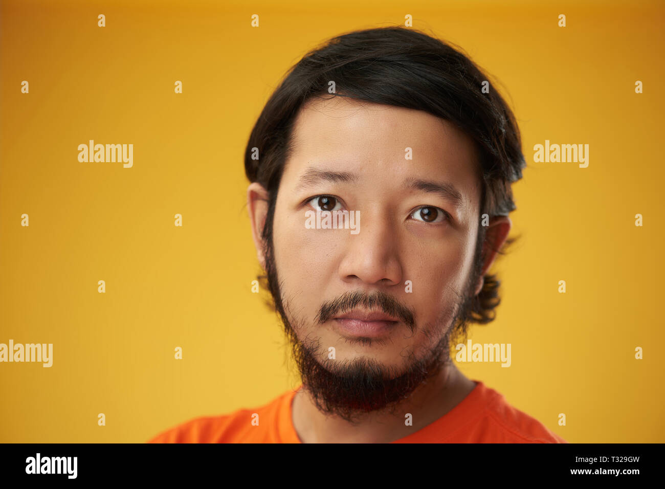 Asian guy headshot isolated on yellow color background. Poker face