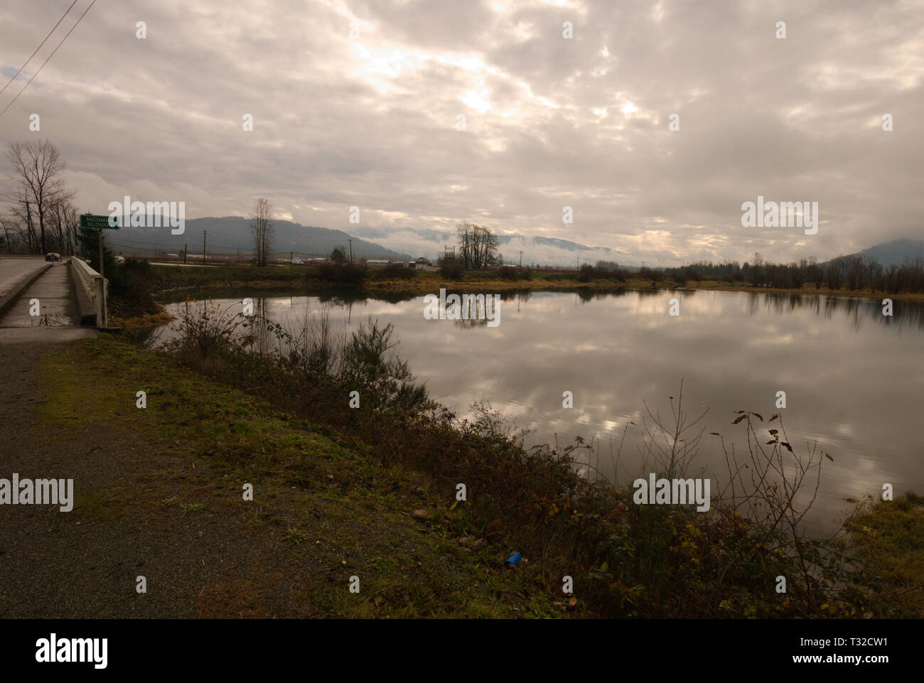 A placid backwater of the Vedder River reflects a turbulent gray overcast sky in Chilliwack, British Columbia, Canada Stock Photo