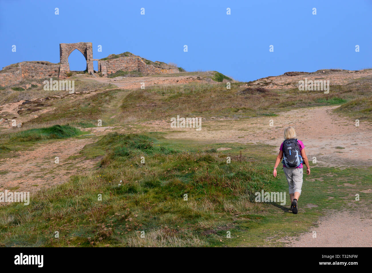 Woman Hiker Walking on Coastal Path to the Ruins of Gronez Castle on the Island of Jersey, Channel Isles, UK. Stock Photo
