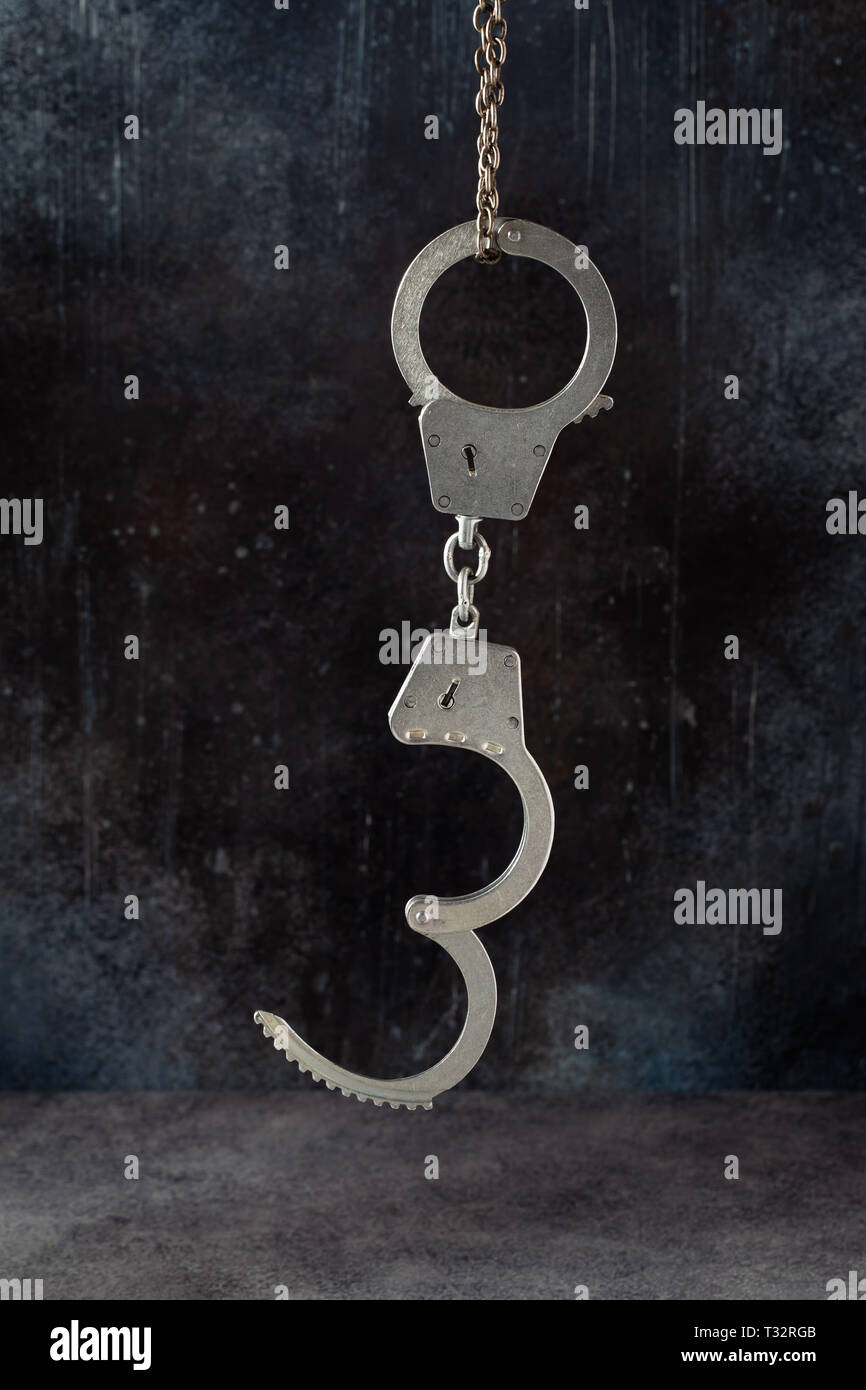 Handcuffs hanging against a grunge dark background Stock Photo