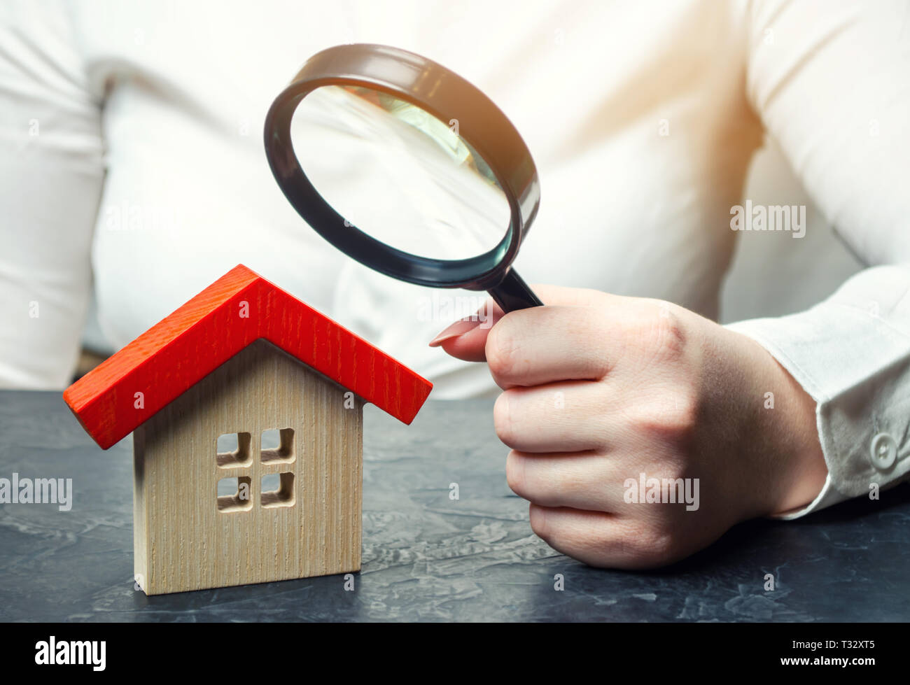 A woman is holding a magnifying glass over a wooden house. Real estate appraiser. Assessment of the condition of the house. Property valuation / appra Stock Photo
