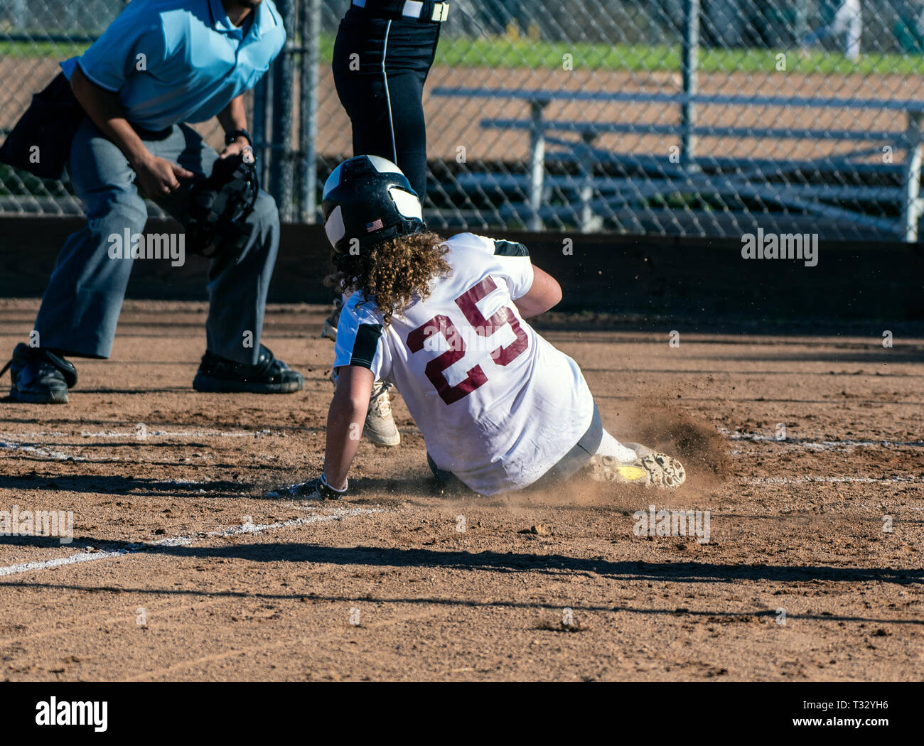 Athletic female softball player sliding safely into home plate under the legs of opponent. Stock Photo