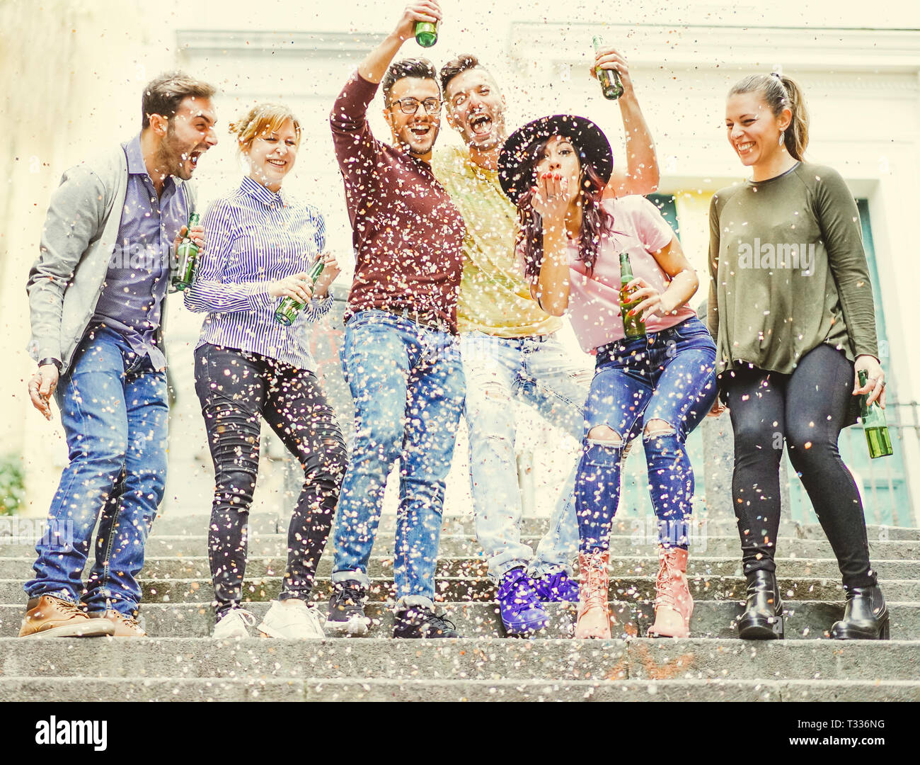 Group of happy friends having a street party drinking beers while confetti are falling down - Hilarious young people celebrating a birthday outdoor Stock Photo