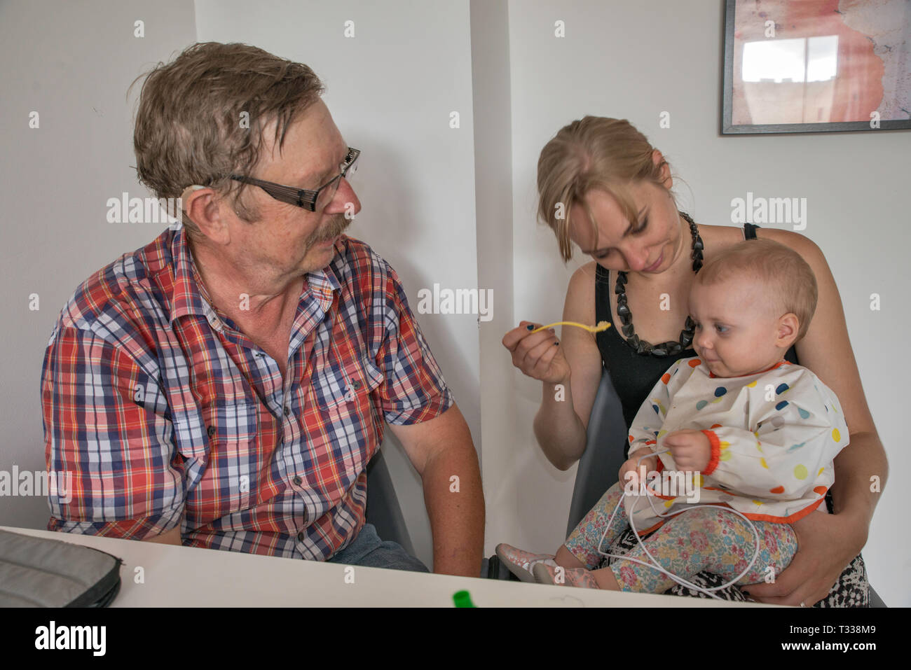 Mother feeding her 1 year old daughter, grandfather Stock Photo