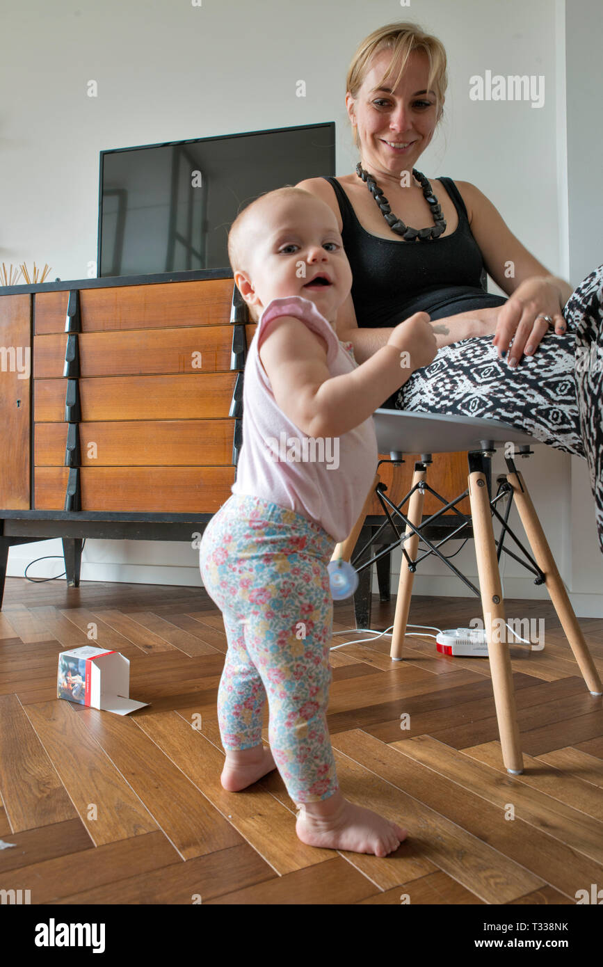 1 year old girl learning to walk, her mother looks on Stock Photo