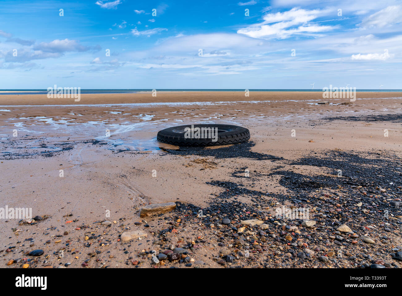 North Sea coast in Cambois, Northumberland, England, UK - and old tyre on the beach with wind turbines in the background Stock Photo