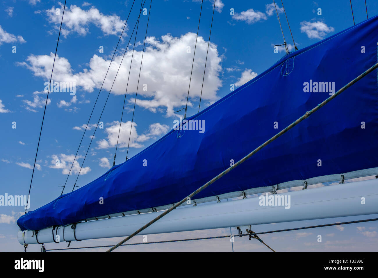 Beautiful bright blue canvas of furles sail against blue sky with white clouds Stock Photo