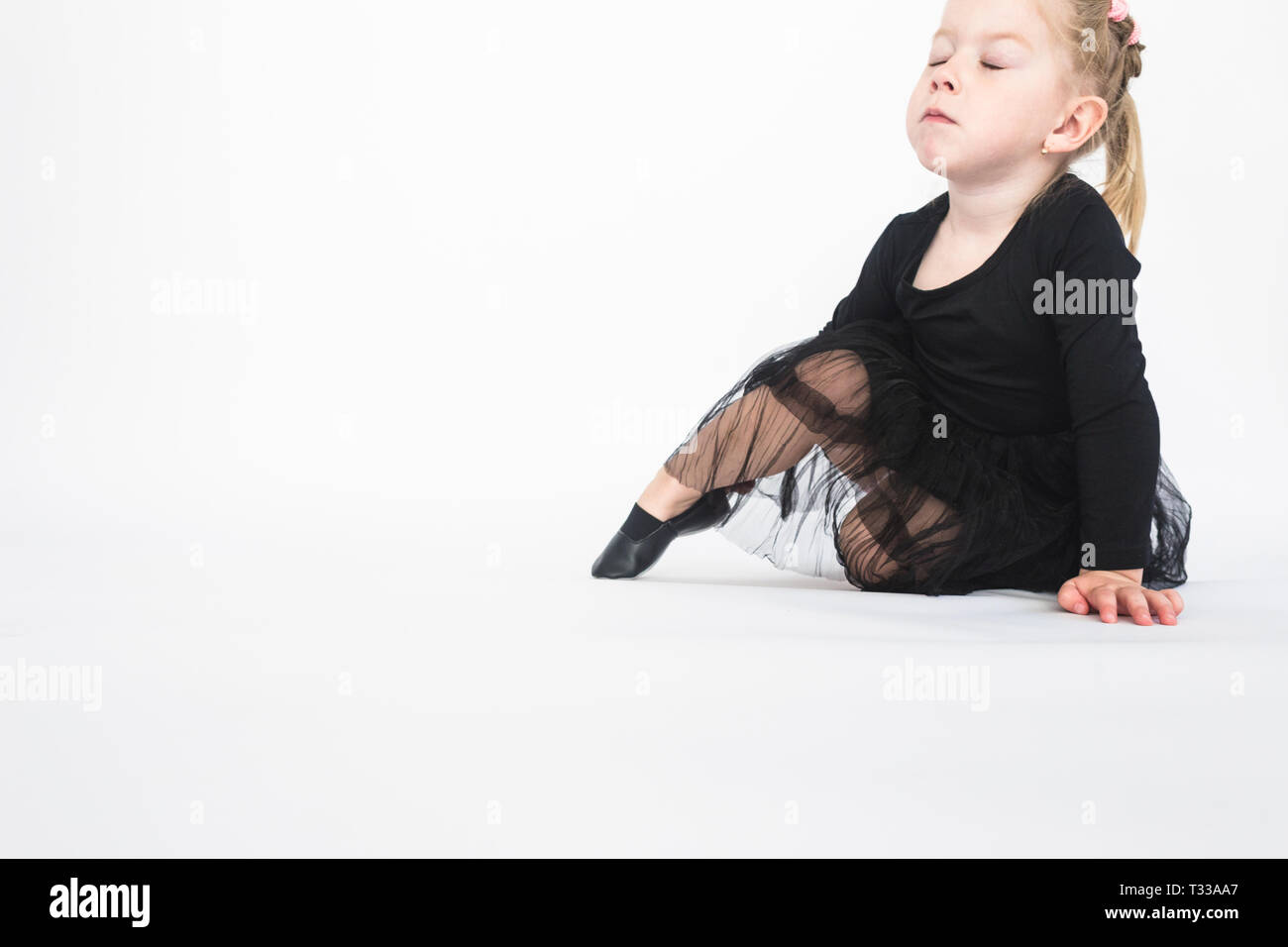 Cute little girl in beautiful black dress sitting on the floor on white ...