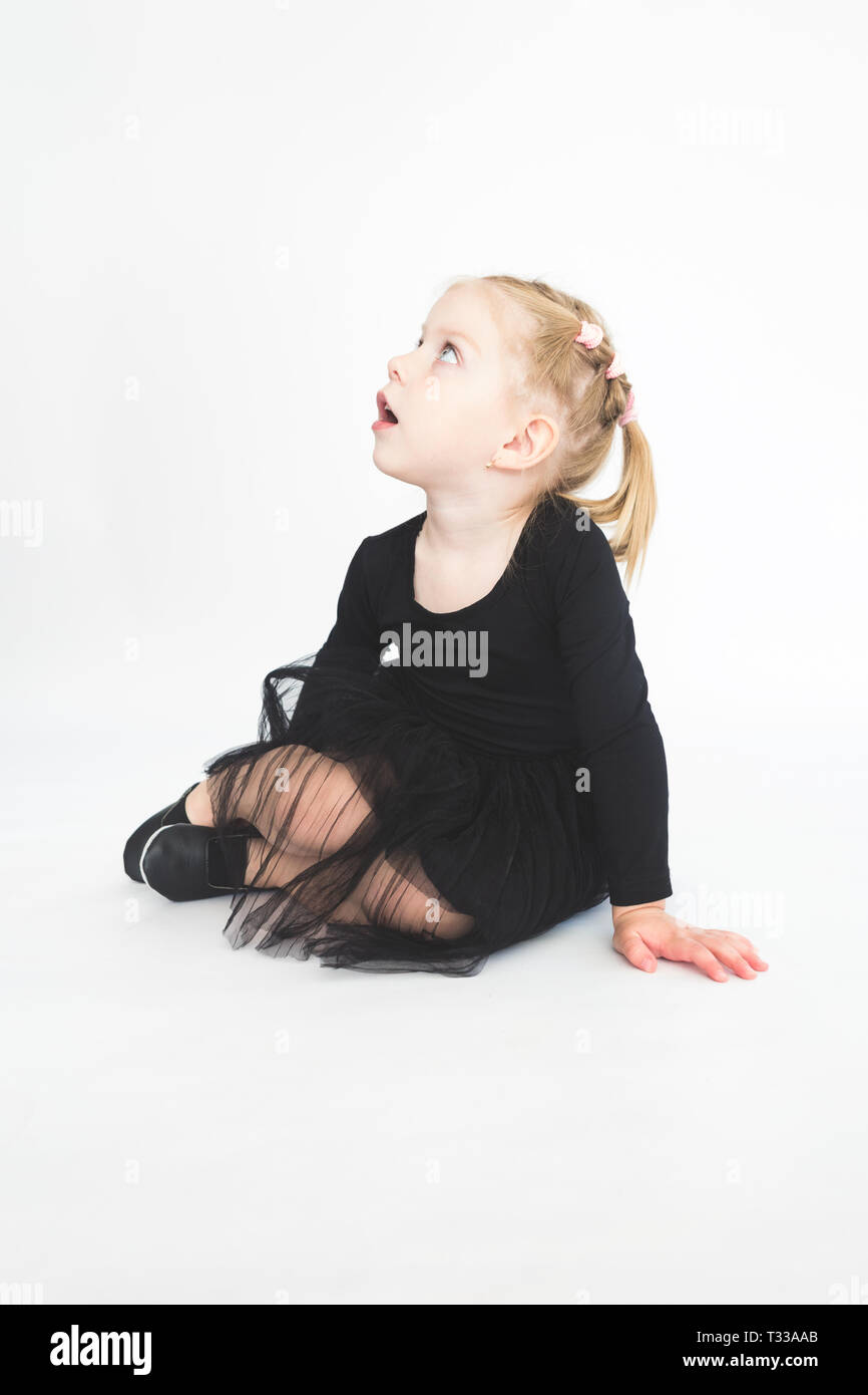 Cute little girl in beautiful black dress sitting on the floor on white ...