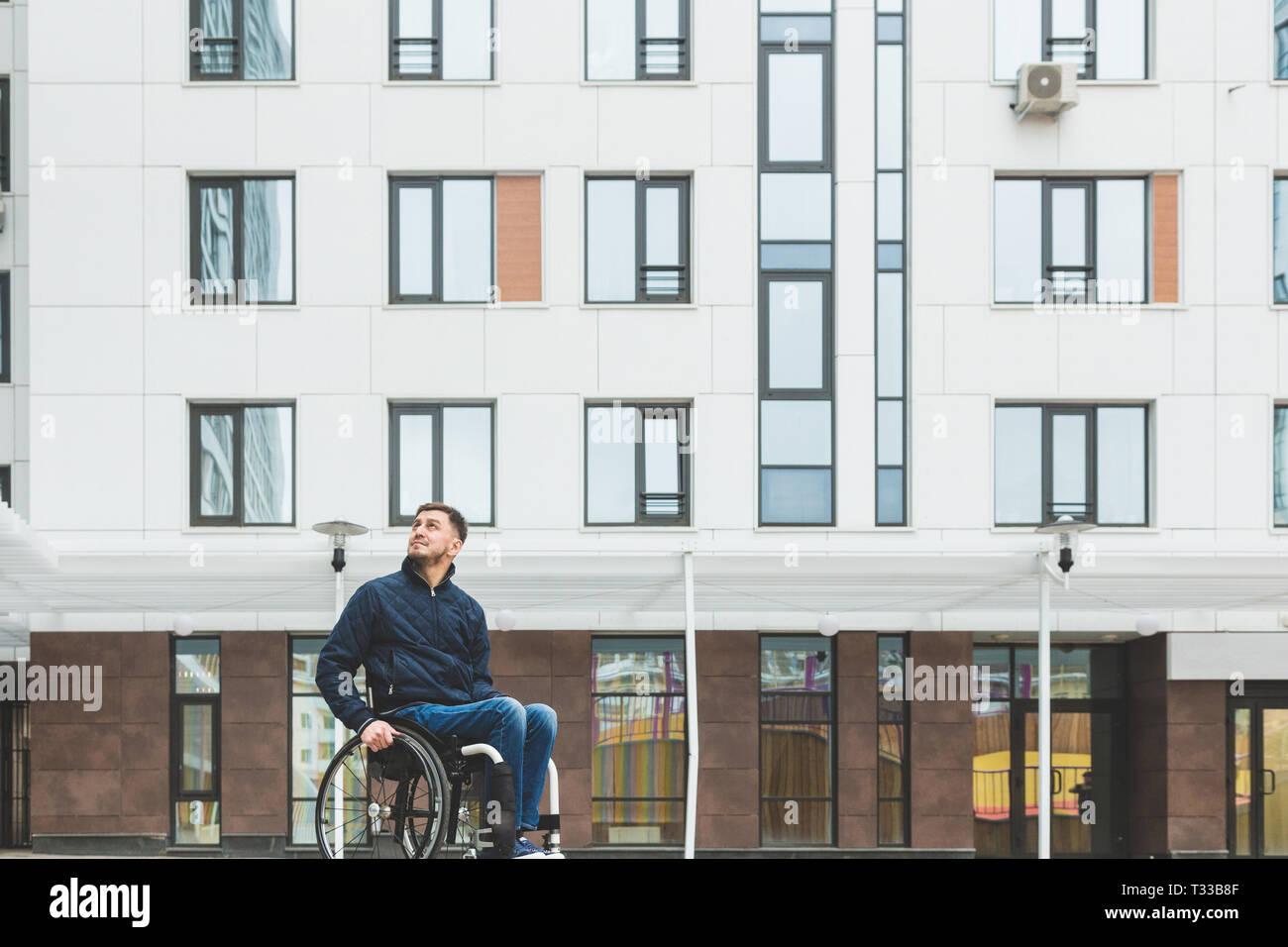 Young man in a wheelchair against the backdrop of a modern high-rise ...