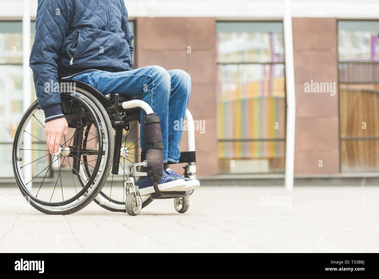 Image showcasing Young man in a wheelchair against the backdrop of a modern high-rise ...