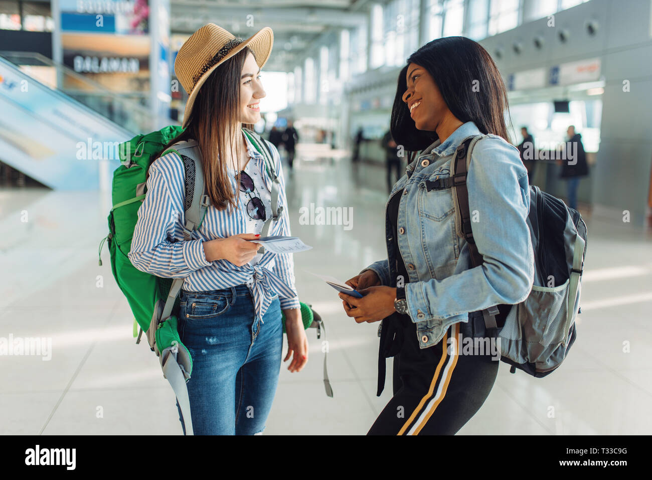 Two female tourists with backpacks in international airport. Passengers with baggage in air