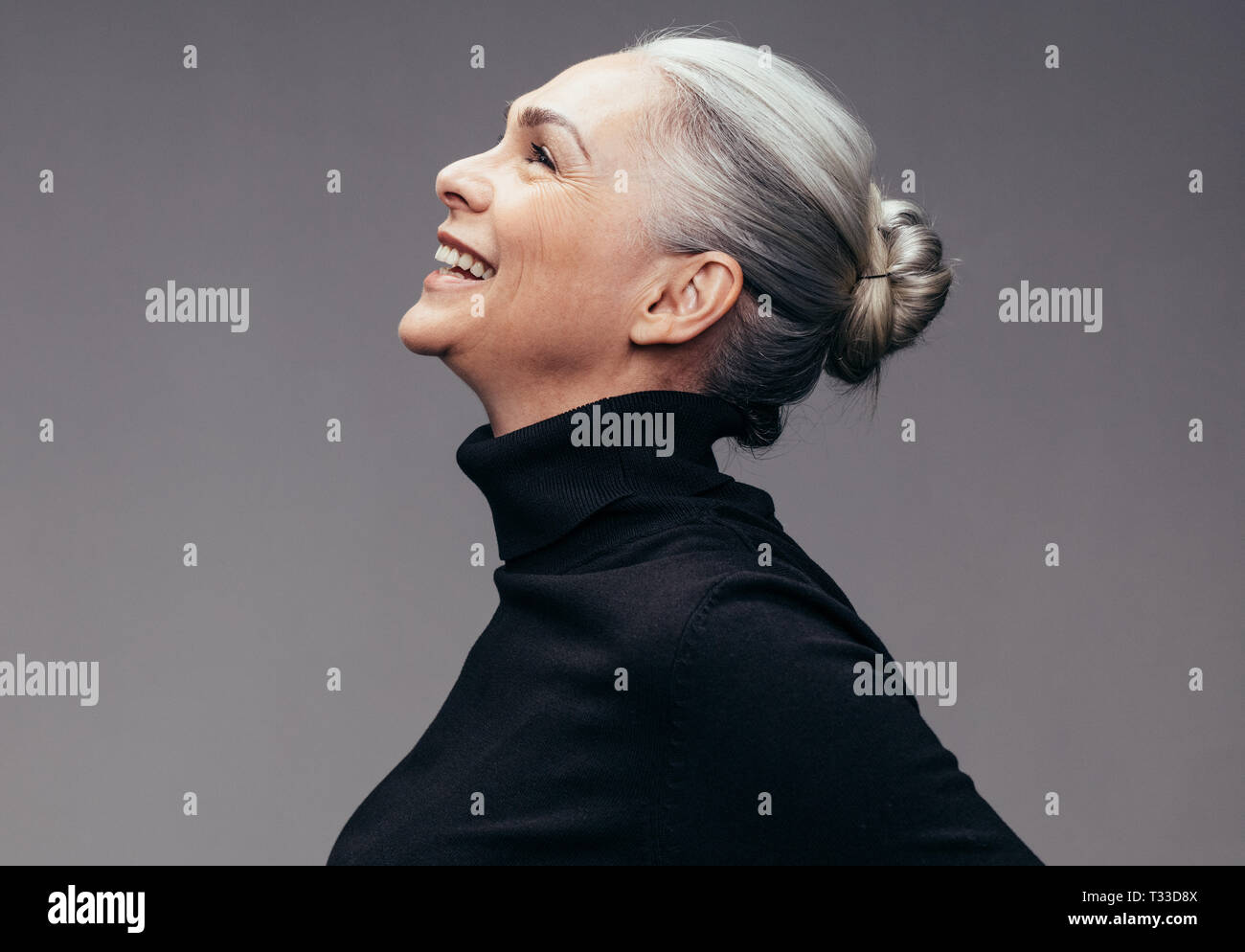 Side view of senior woman laughing on gray background. Profile view of mature woman in black casuals looking happy Stock Photo