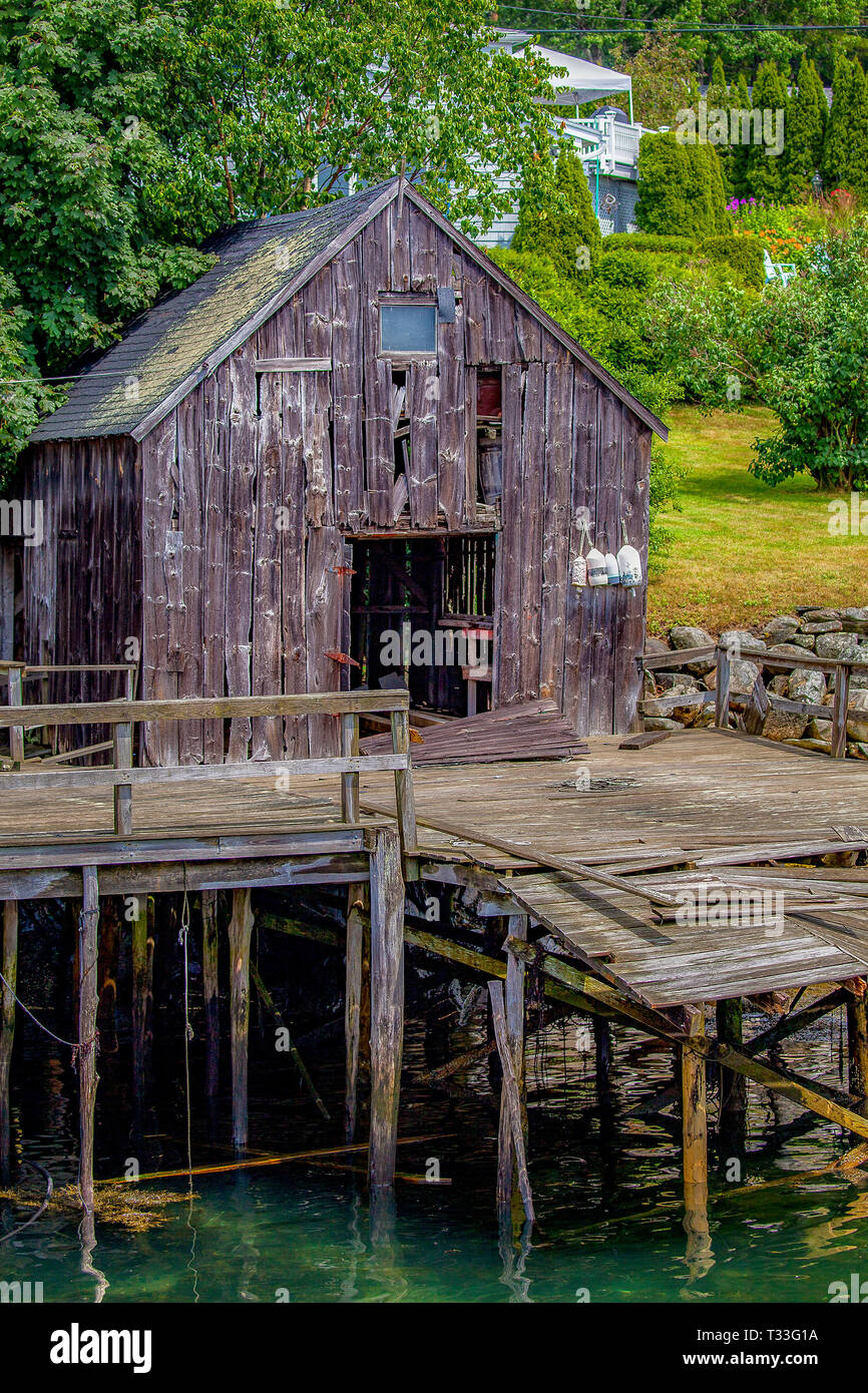 An old, wooden, severely weathered seaside shanty standing on a dock held with piers is in process of collapsing in New Harbor, Maine, USA. Stock Photo