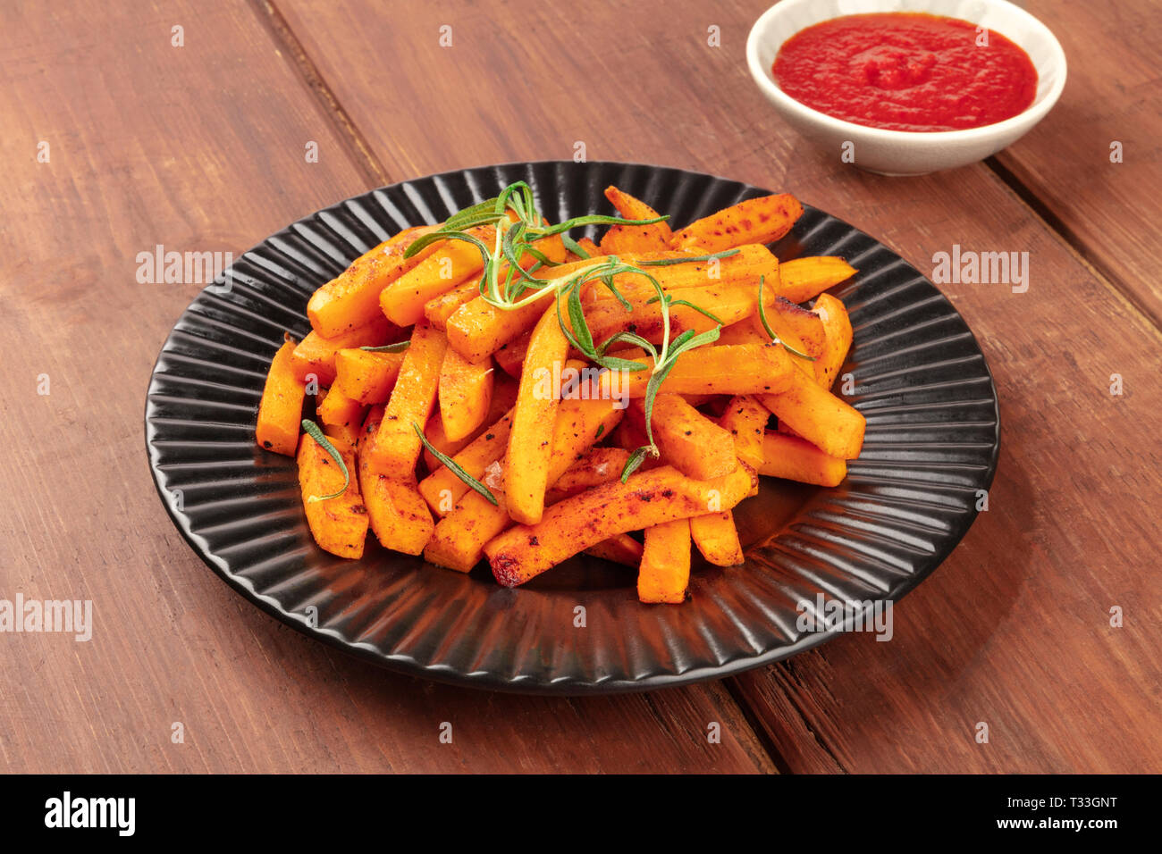 Sweet potato fries with rosemary and ketchup on a dark rustic wooden background Stock Photo