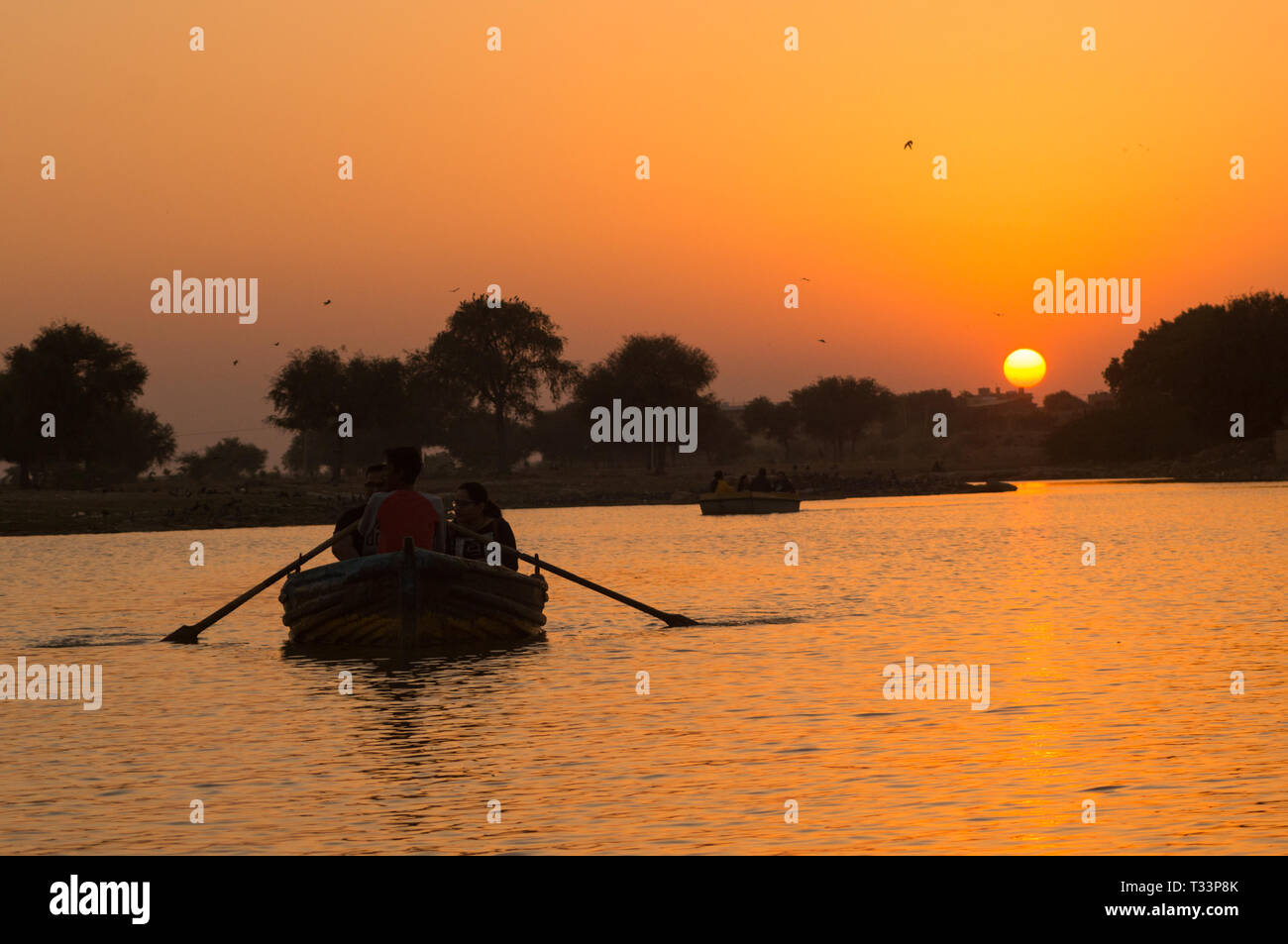 People taking a boat ride on Gadi Sagar lake in Jaisalmer at sunset with the sun in the background Stock Photo