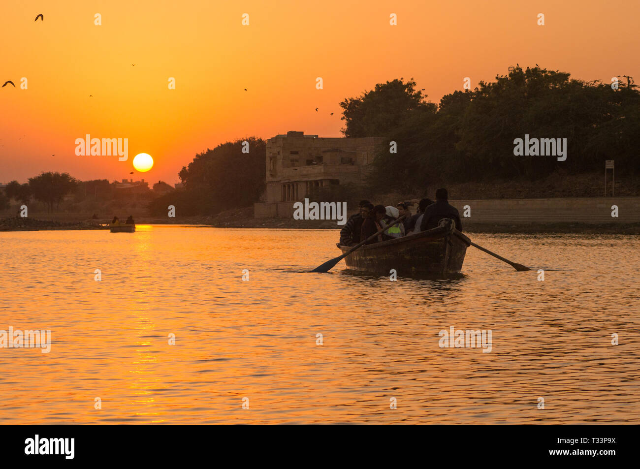 People taking a boat ride on Gadi Sagar lake in Jaisalmer at sunset with the sun in the background Stock Photo