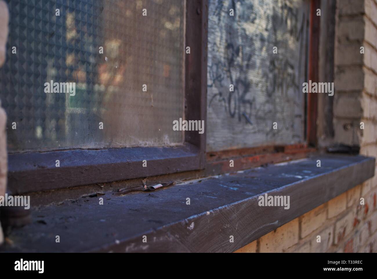close up of a broken boarded up window and sill with peeling paint and