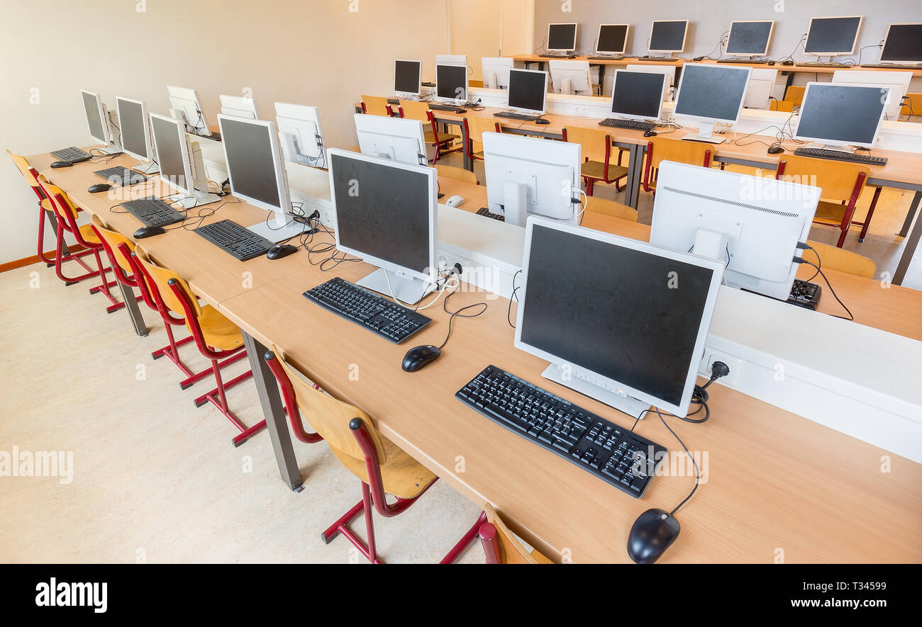 Computer class with rows of desktop computers tables and chairs in high school Stock Photo