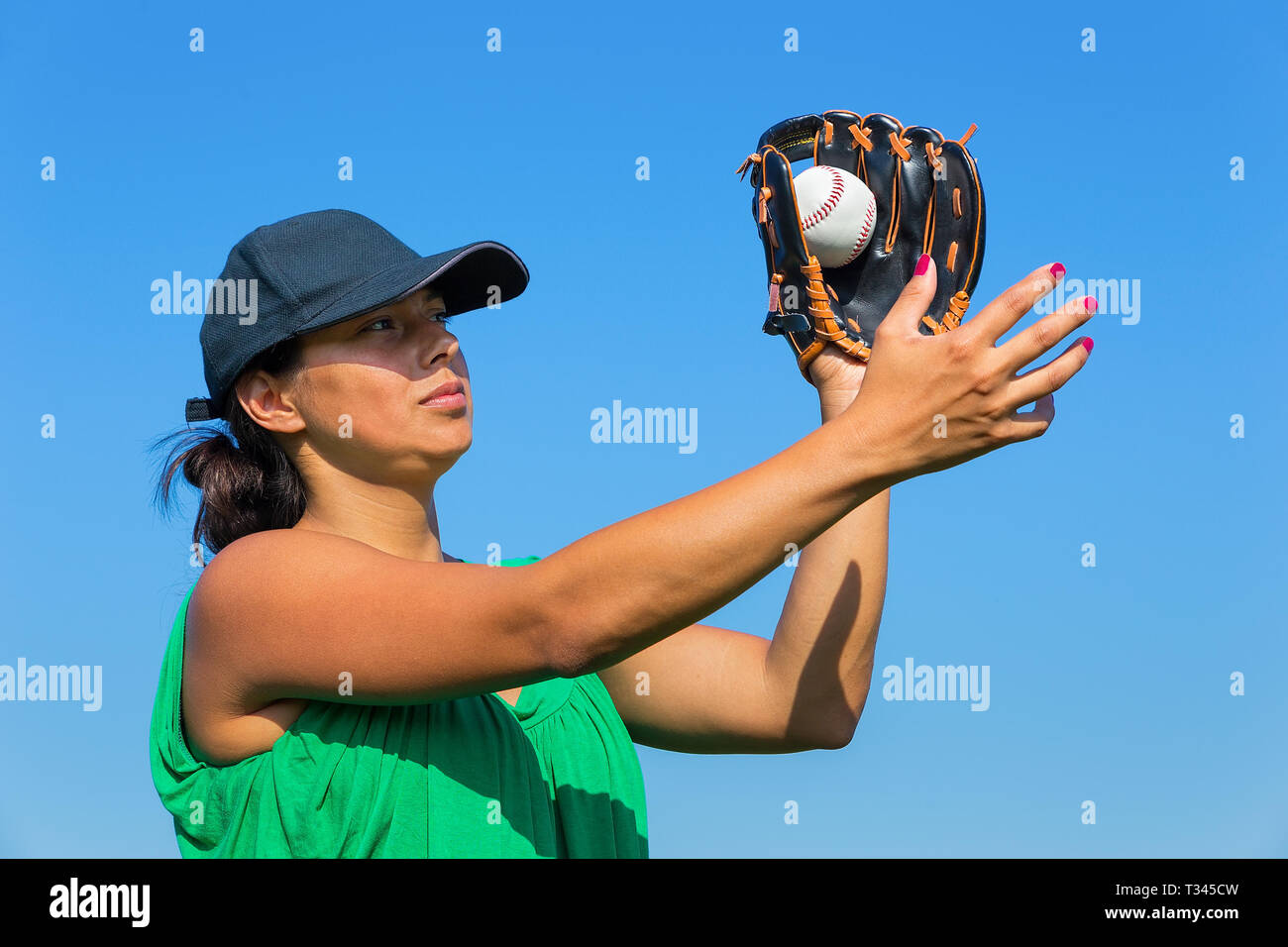 Colombian woman with glove and cap catching baseball outdoors with blue sky Stock Photo