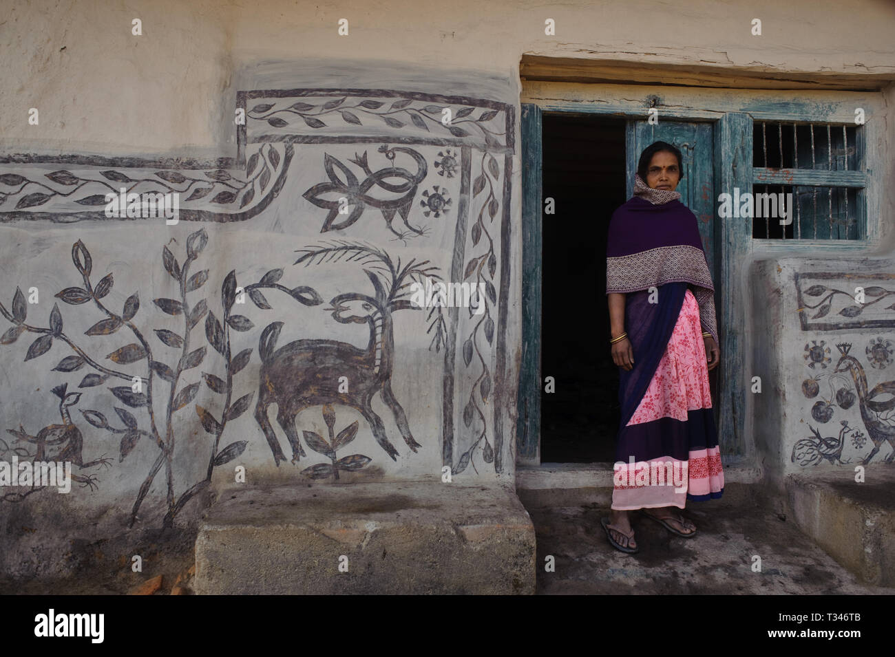 Low caste woman standing in front of her house decorated with mural paintings ( India). This art form is called Khovar art. Stock Photo