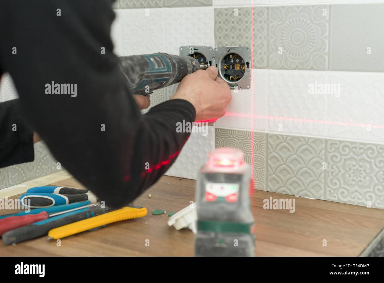 Electrician using infrared laser level to install electrical outlets