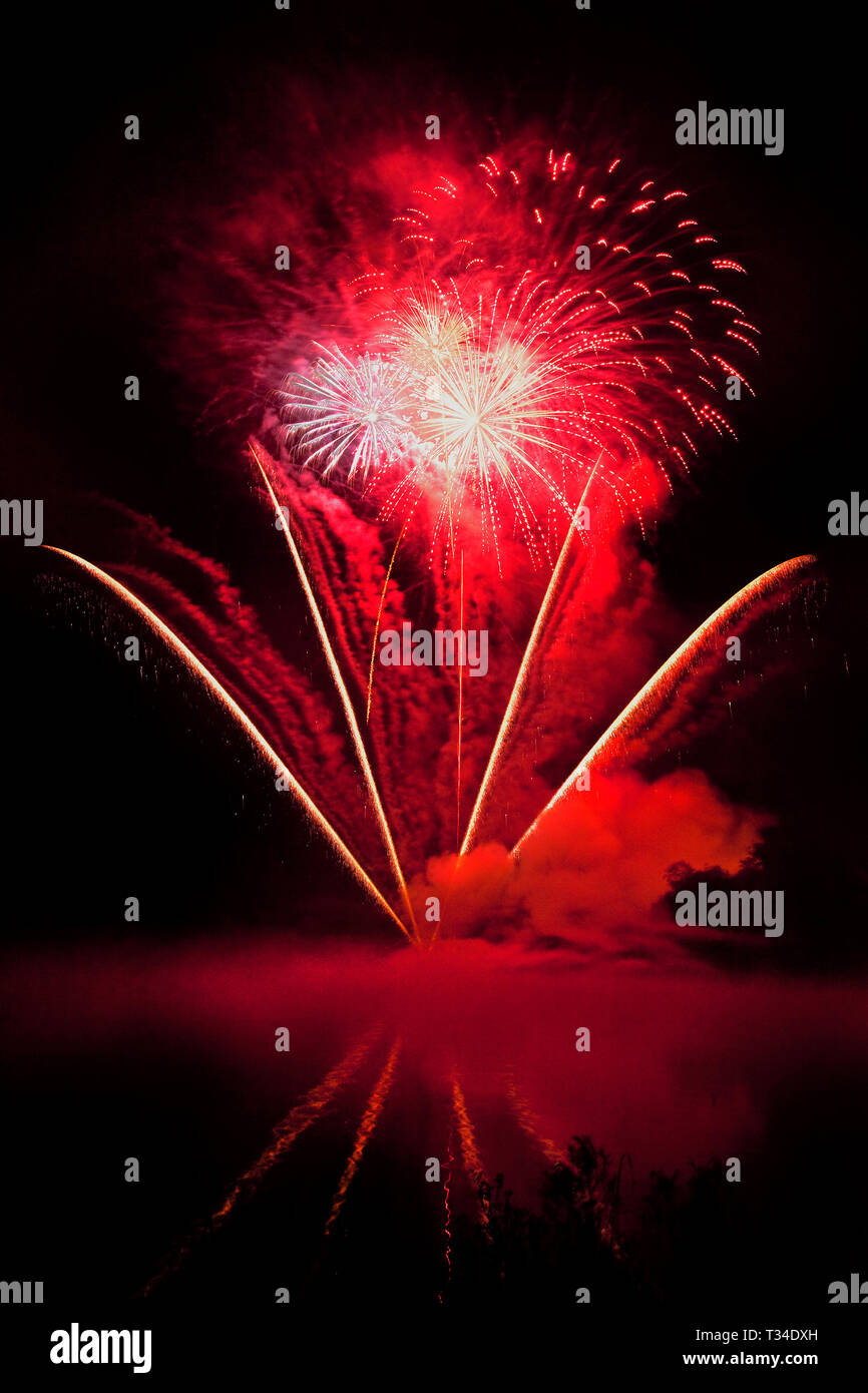 Spectacular commercial fireworks light up the sky with vibrant colour refelctions in a foreground lake - artistic light pattern. Stock Photo