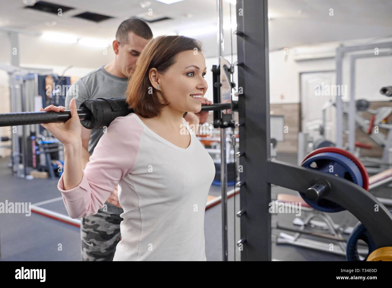 Mature woman doing sport exercises with personal trainer at gym. Male instructor assisting older woman. Stock Photo