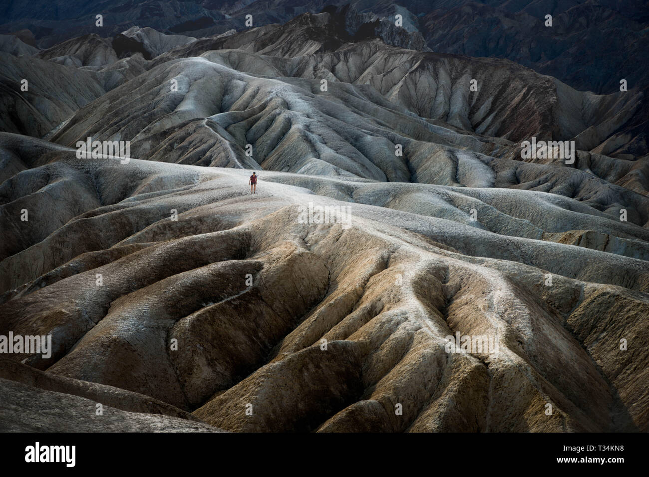 Woman walking along the rim of the Badlands, Death Valley, California, United States Stock Photo