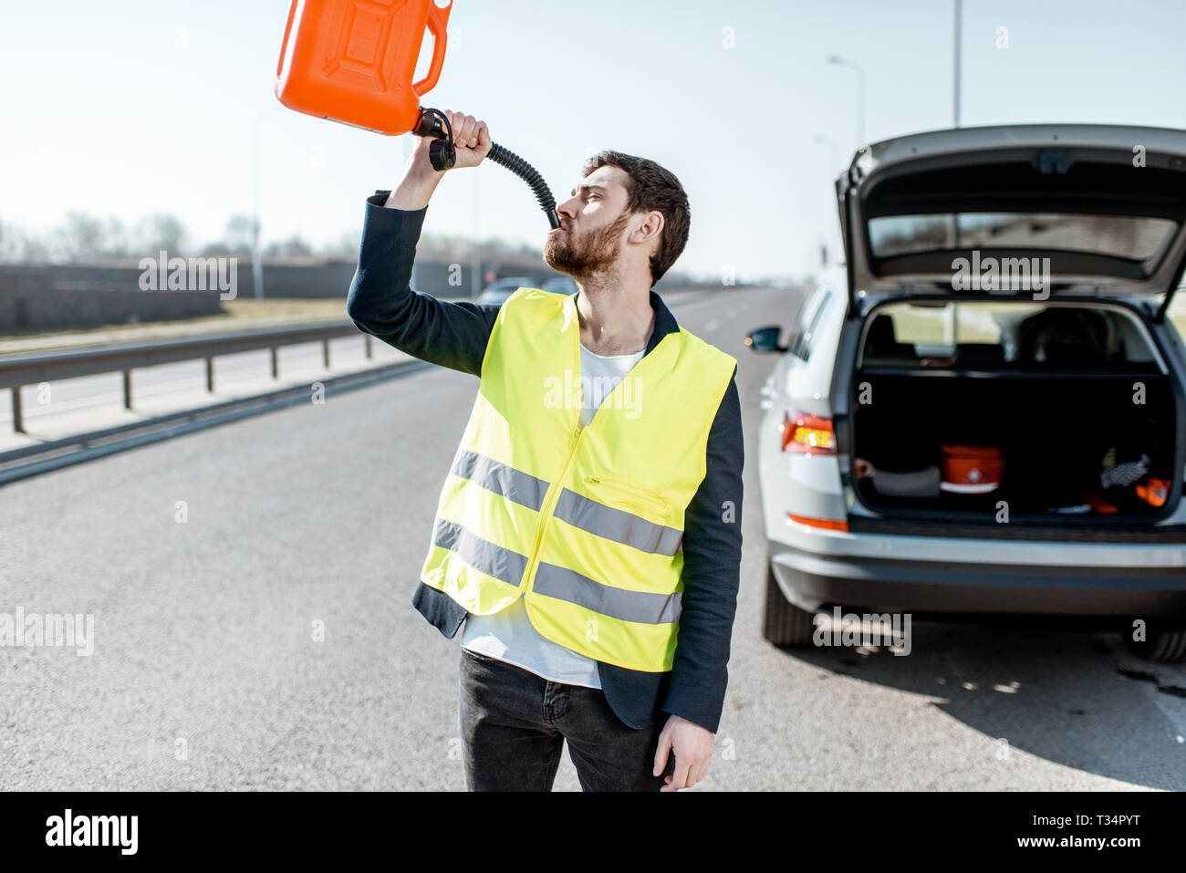 Funny portrait of a man drinking from the refuel can near the broken car on the roadside Stock Photo