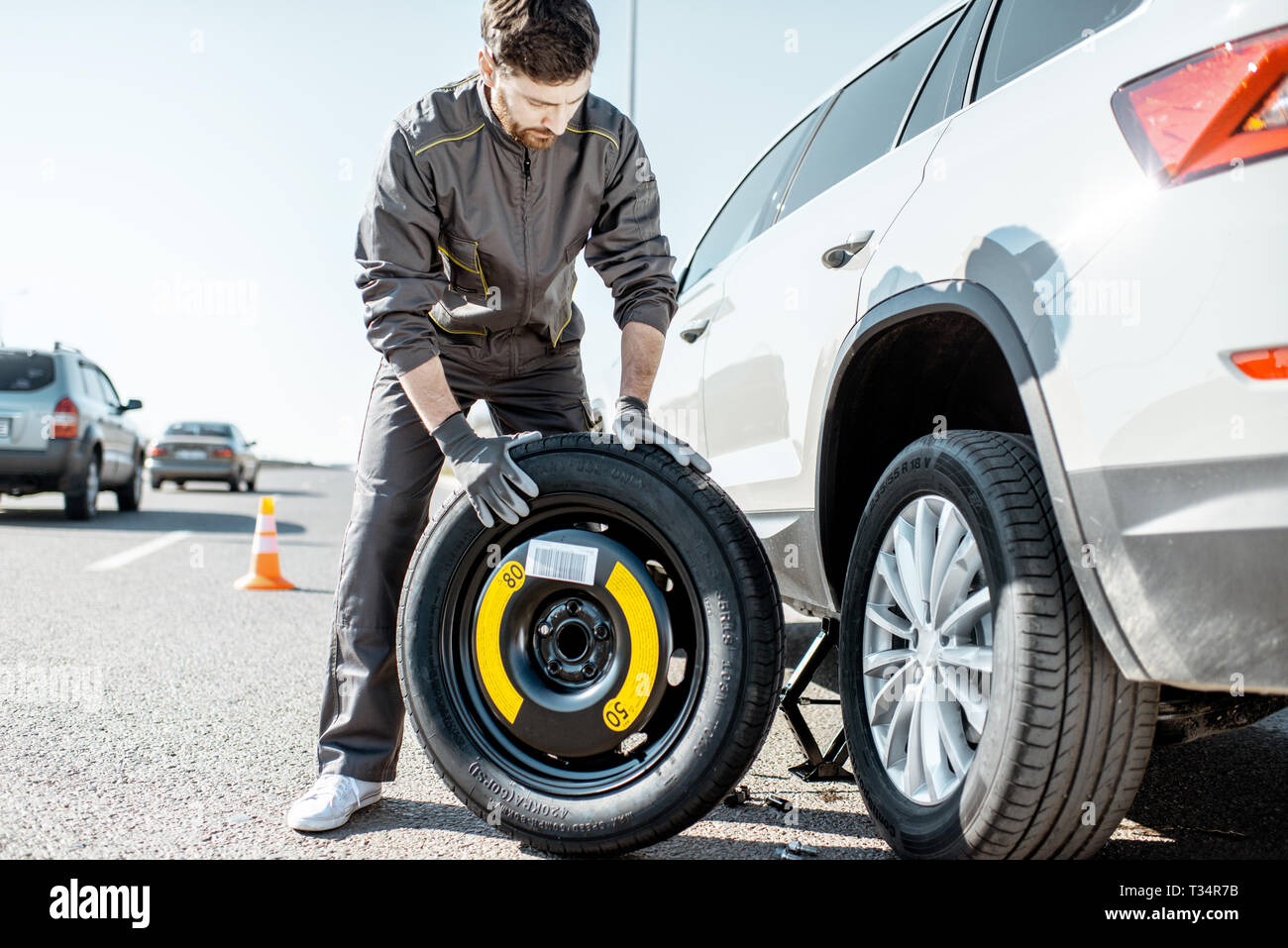 Road assistance worker in uniform changing car wheel on the highway Stock Photo