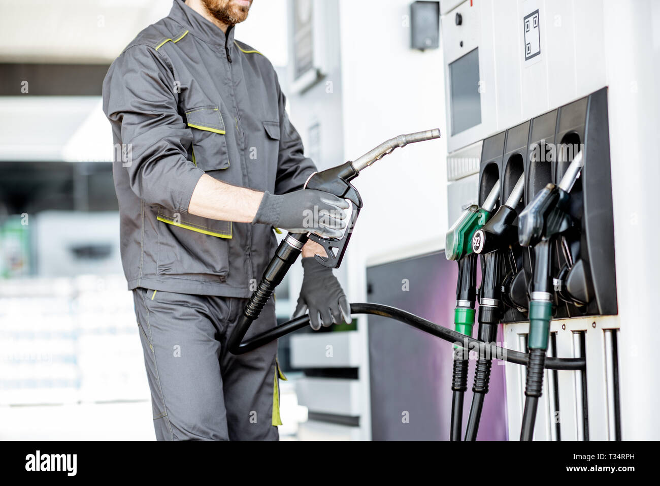 Gas station worker in uniform taking filling gun, refueling car at the