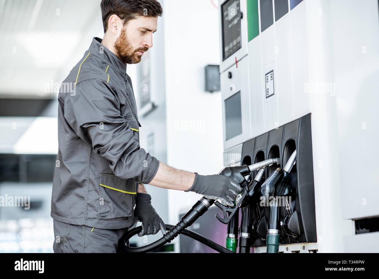 Gas station worker in uniform taking filling gun, refueling car at the ...