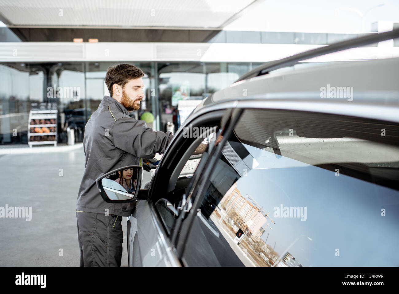 Gas station worker in uniform washing car windshield at the station