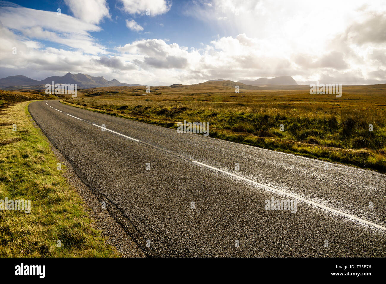 Sunlight pierces cloud over a curve in the A836 road with mountains Ben ...