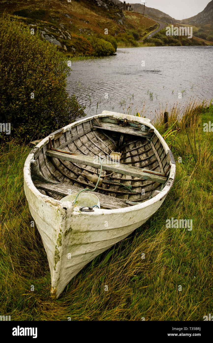 A derelict wooden rowboat sits on the shore of Loch Dubh in Tarbet, on the west coast of Scotland. Stock Photo