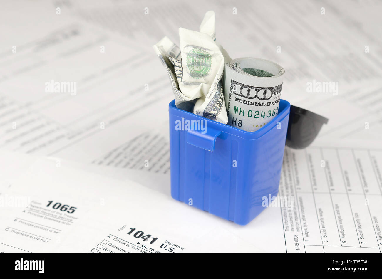 Many american tax blank forms and crumpled hundred dollar bill in trash