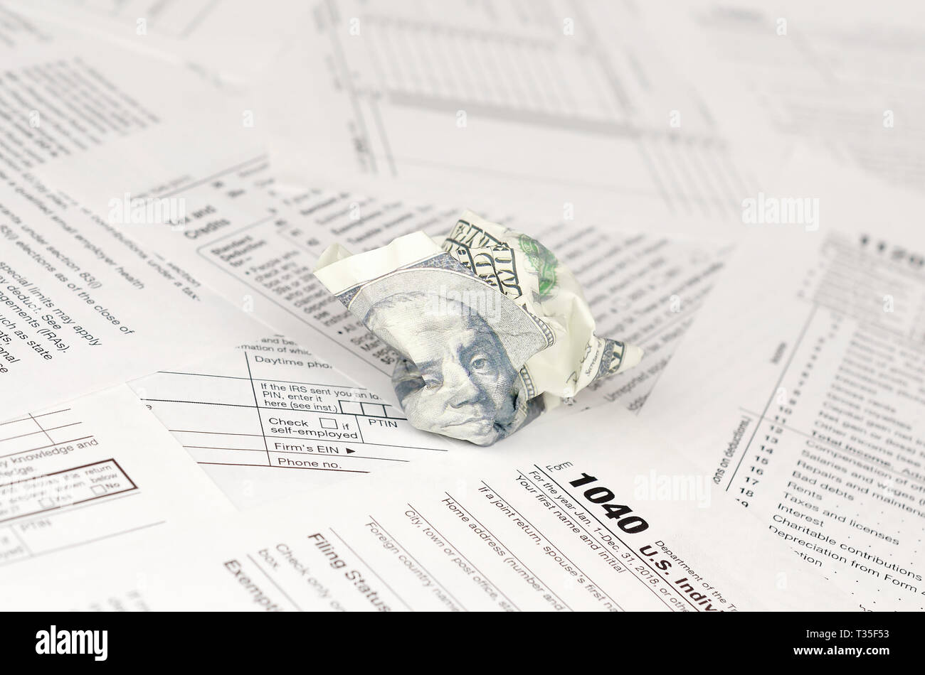 1040 Individual tax return form and crumpled hundred dollar bill. Loss of money to pay