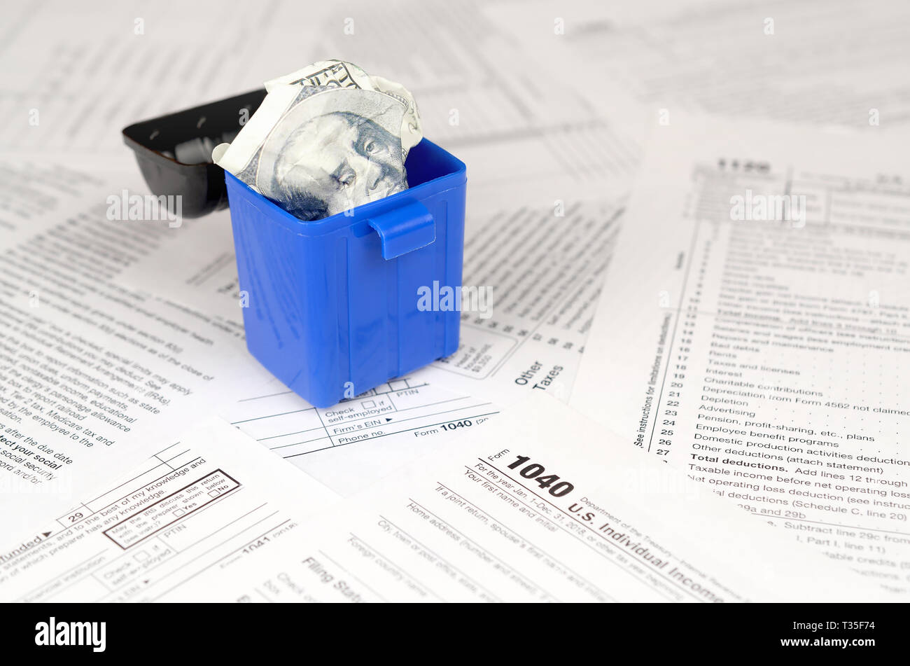 Many american tax blank forms and crumpled hundred dollar bill in trash