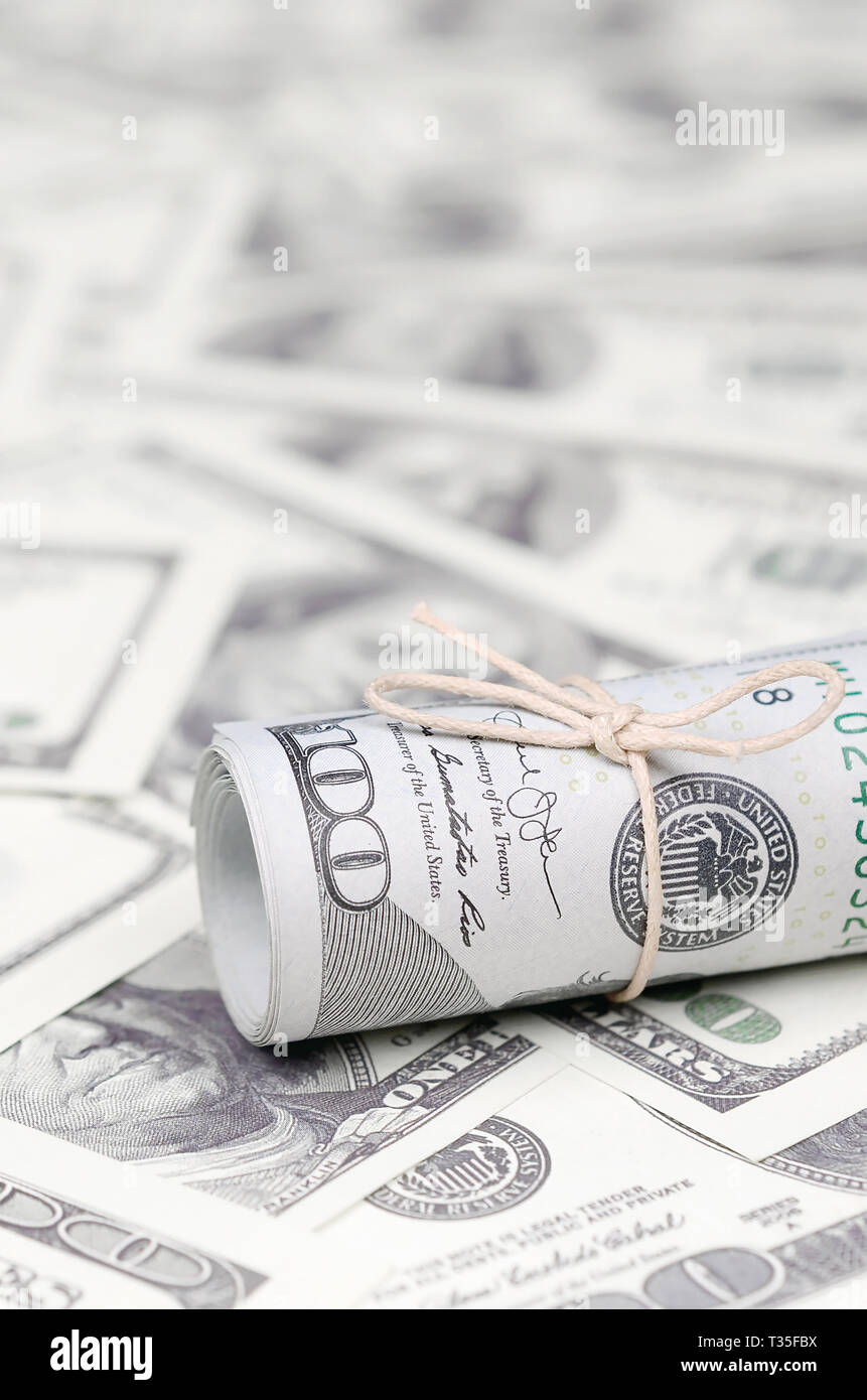 US dollars rolled up and tightened with band lies on a lot of american banknotes with blurred