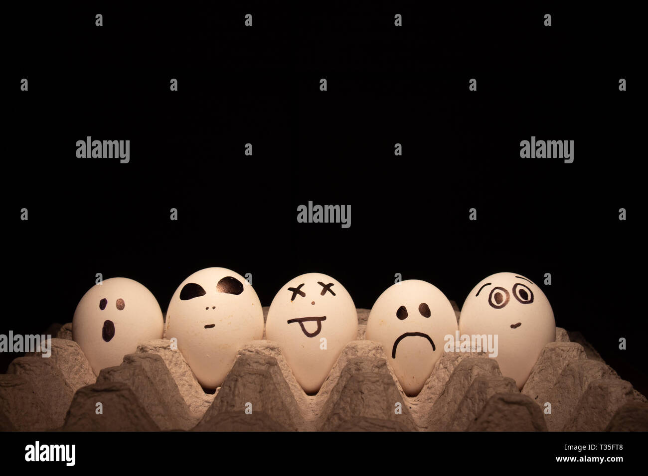 Chicken or Easter eggs with funny faces on black background. Stock Photo