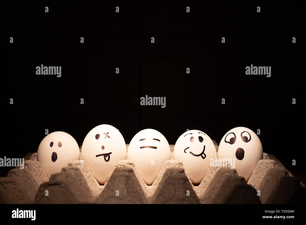 Chicken or Easter eggs with funny faces on black background. Stock Photo