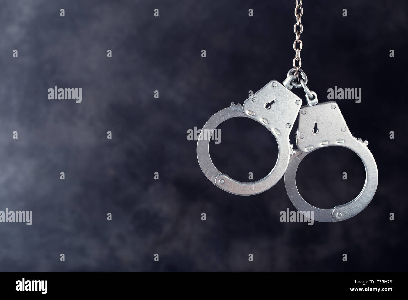 Handcuffs hanging against a dark background with copy space Stock Photo