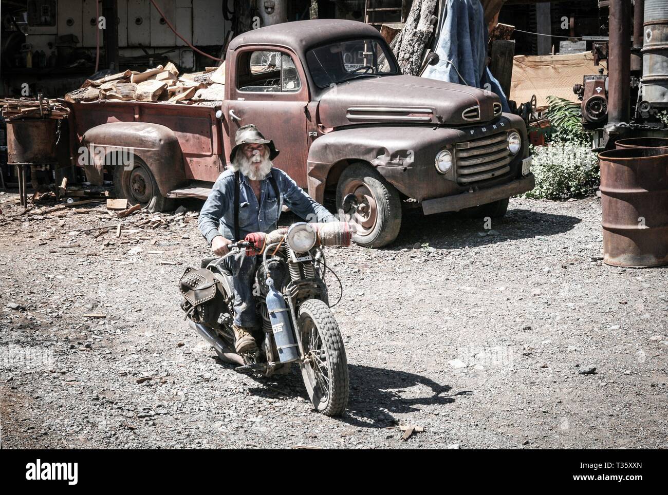 bearded old timer rides vintage motorcycle in front of old flatbed truck usa mining museum Stock Photo