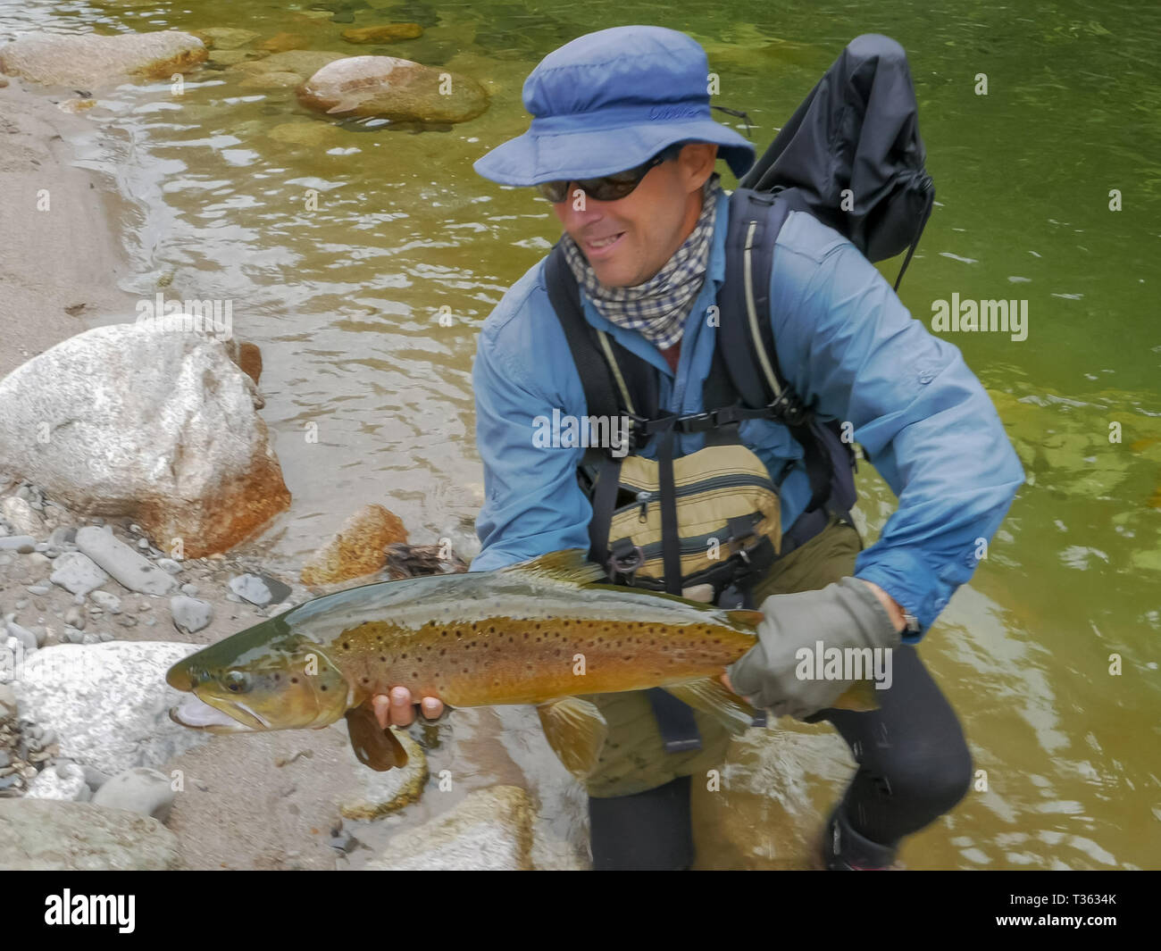 a fly fisherman with a large brown trout caught in a clear new
