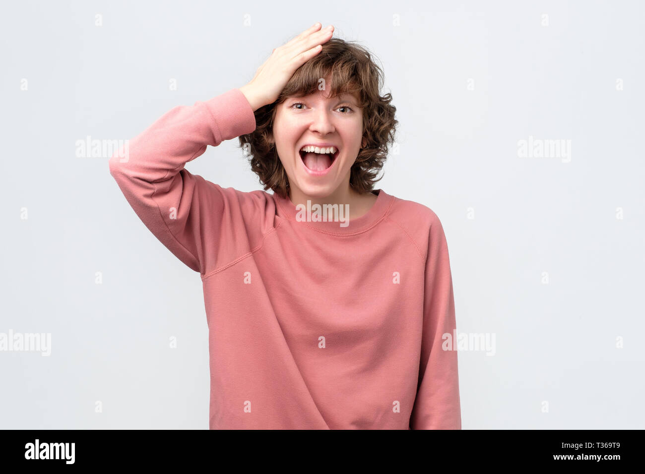 Forgetful young woman holding hand on her head struggling to remember something. Cute curly female student slapping forehead Stock Photo