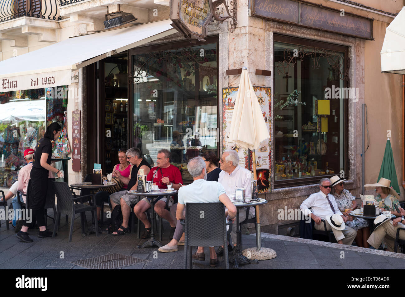 Cafe culture - people sitting at pavement cafeteria in Corso Umberto I in the city of Taormina, East Sicily, Italy Stock Photo