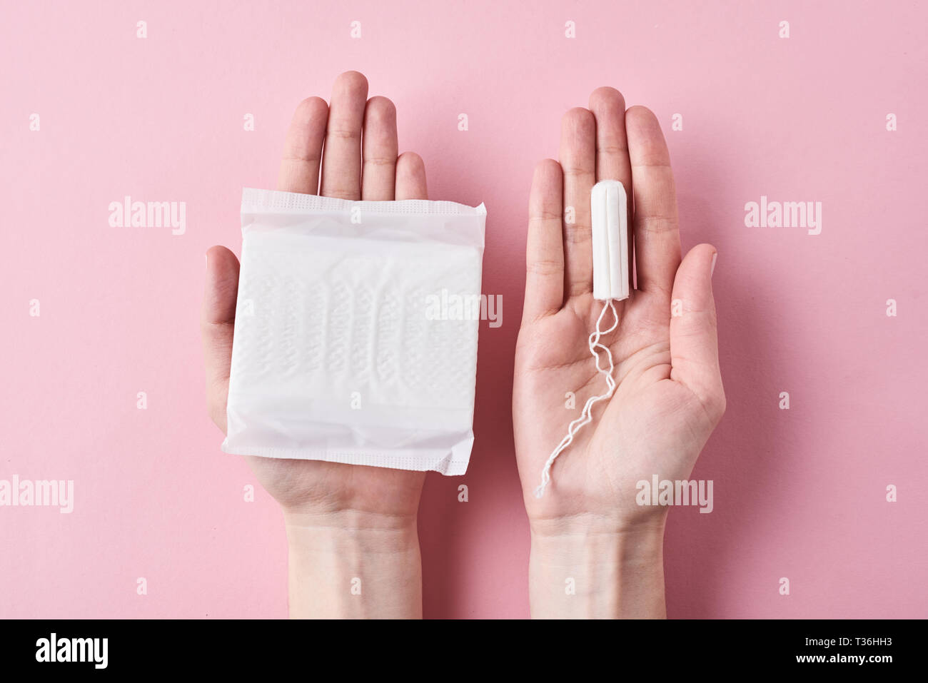 Woman hands hold sanitary pad and tampon on pink background Stock Photo