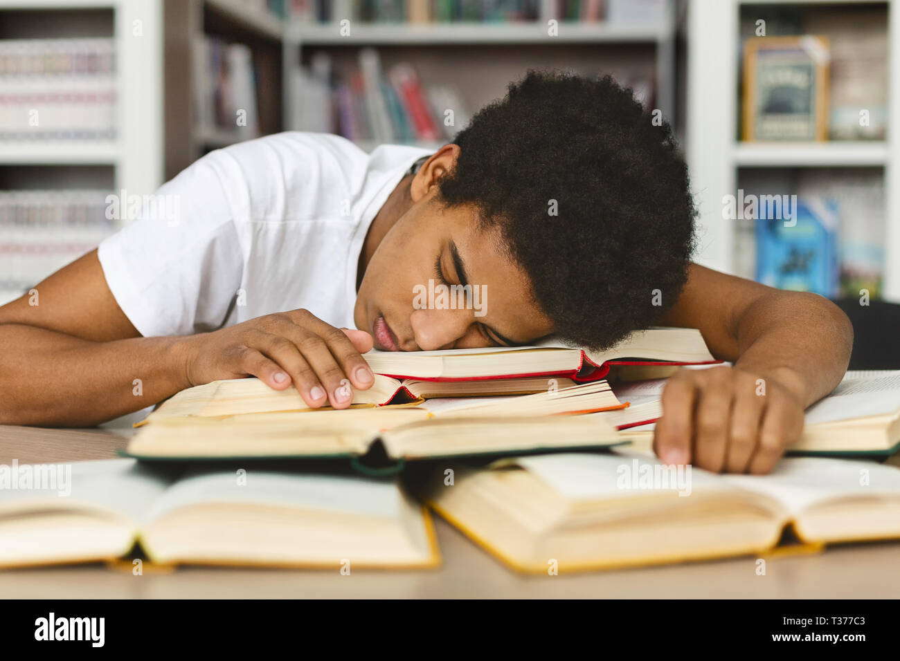Tired guy napping on books stack in library Stock Photo