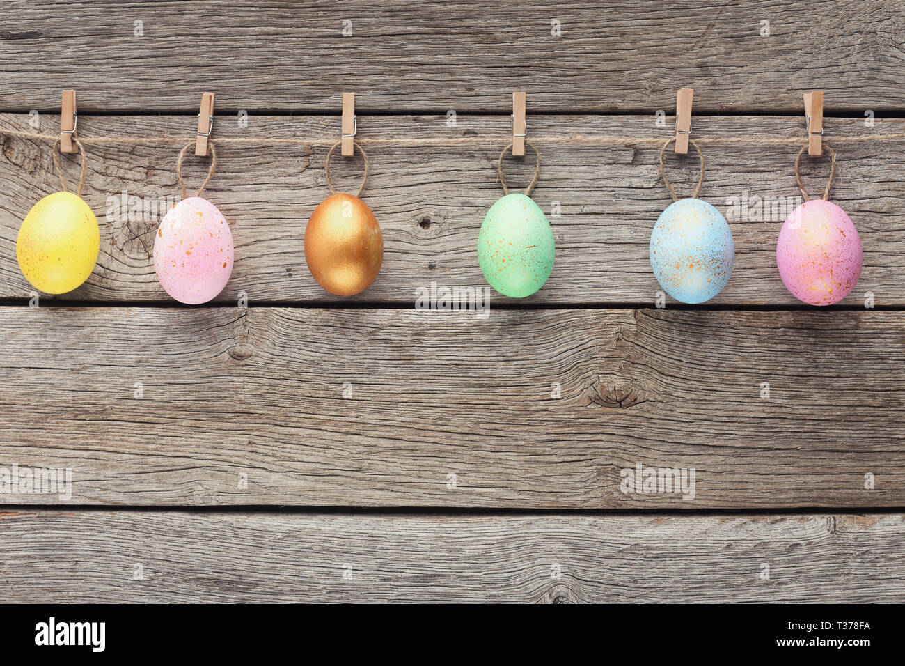Colourful quail eggs attach to rope with clothes pins on wooden background, copy space Stock Photo